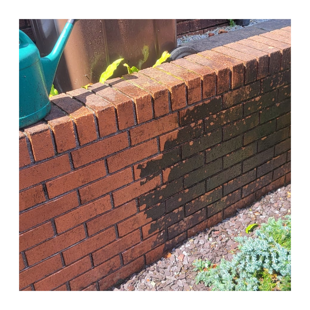 a red brick wall with a green watering can on top. The wall is dirty but has been power washed so the red brick is clean on the left but black and dirty on the right.