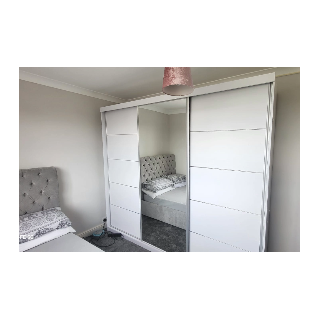 A bad with a grey velvet headboard and a large white panelled wardrobe.